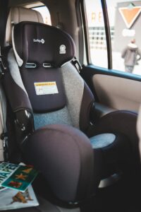 Travel car seat for babies placed on passenger seat of contemporary automobile with magazines near window parked on street of city