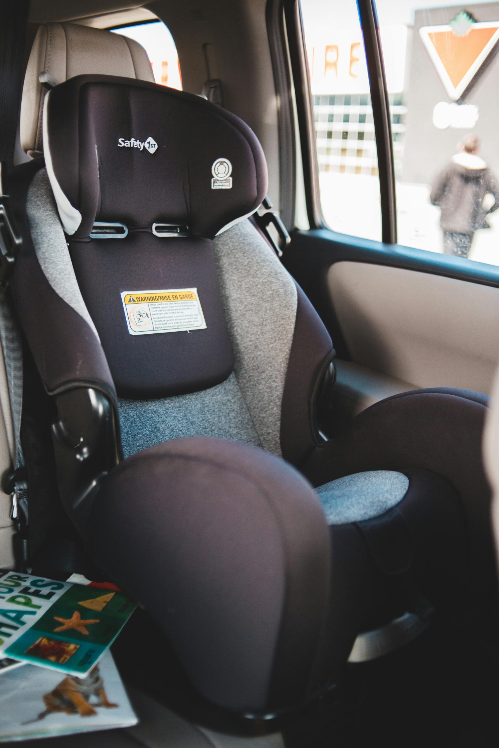 Travel car seat for babies placed on passenger seat of contemporary automobile with magazines near window parked on street of city